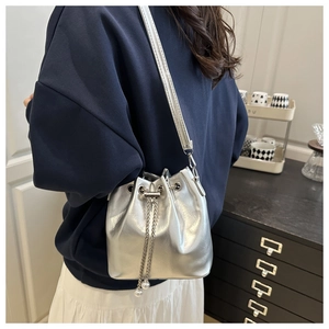 Silver metallic bucket bag with pearl drawstring detail worn by a model in a side view