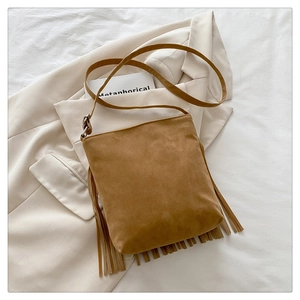 Detail of brown suede shoulder bag with long fringes over a beige blazer jacket