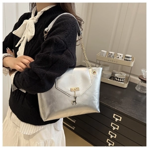 Detail of silver tote bag featuring gold chain strap and metal deer charm pendant