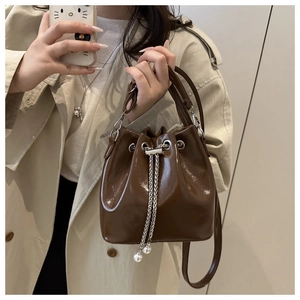 Detail of dark brown glossy bucket bag with pearl chain drawstring and silver accents