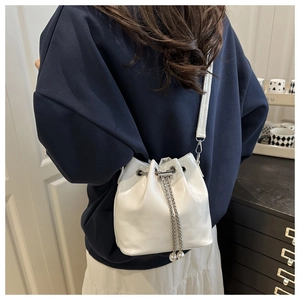 Detail of white glossy leather bucket bag with silver chain and pearl charms on shoulder