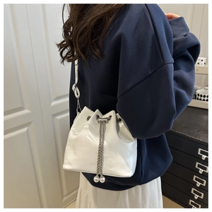 Detail of white glossy patent leather bucket bag with silver chain and large pearl charms