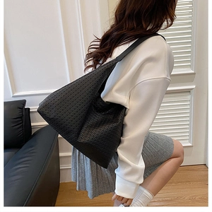 Side view of large black woven shoulder tote bag worn by a model in a minimalist room