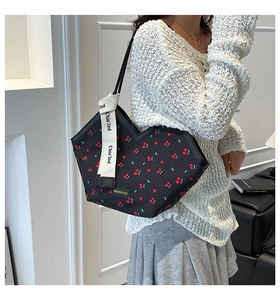 Detail of black canvas tote bag with red cherry prints and decorative logo ribbon