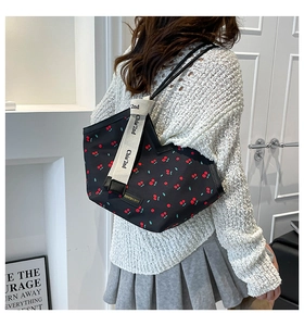 Detail view of black tote bag with red cherry print and wide branded white shoulder strap