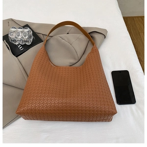 Detailed view of brown woven leather hobo bag on a bed with lifestyle props