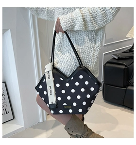 Detail of black tote bag with white polka dots and v-shaped opening showing the logo strap