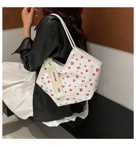 Detail of white bucket bag with cherry print and branded strap worn by a model