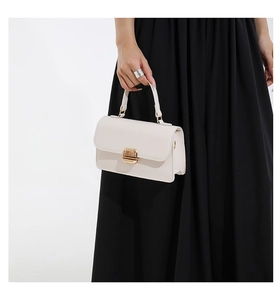 Detail of creamy white leather crossbody bag with elegant gold twist-lock and handle