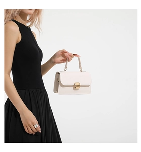 Detail of minimalist white rectangular handbag with gold metal clasp held by model
