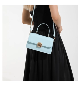 Detail of light blue crossbody bag with gold lock buckle and adjustable shoulder strap