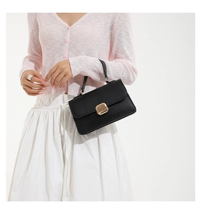 Detail of elegant black oil-wax leather handbag with gold metal clasp on a stylish model