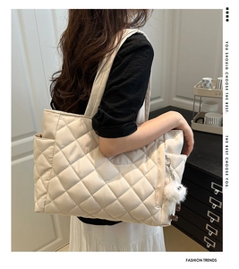 Close-up of beige quilted tote bag featuring a plush ball charm and convenient side pocket