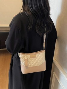 Quilted beige and tan shoulder bag with patterned strap shown on a model
