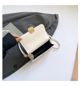 Macro detail of beige crossbody bag with gold circular clasp on a grey suit jacket