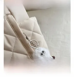 Detail of beige quilted tote bag featuring a cute white furry monster bag charm accessory