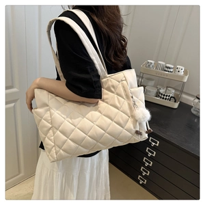 Detail of off-white quilted tote bag with wide shoulder strap and plush pompom accessory
