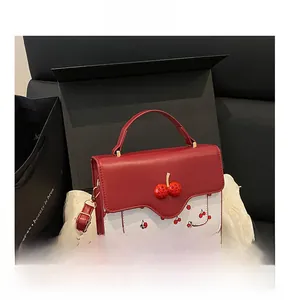 Close-up of cherry pattern handbag with golden metal hardware and red flap in a gift box