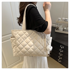 Close-up of beige quilted tote bag with side pocket and plush monster charm on shoulder