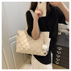 Detail view of beige quilted tote bag featuring a diamond pattern and white plush pendant