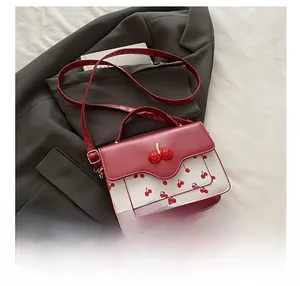 Detail of red cherry metal charm on a white floral crossbody bag with wavy flap design