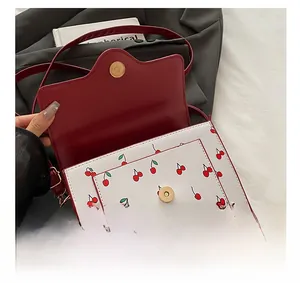 Detail view of gold magnetic snap button and red cherry print on contrast shoulder bag