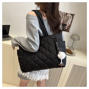 Close-up of black quilted tote bag with side pocket and plush white pompom charm