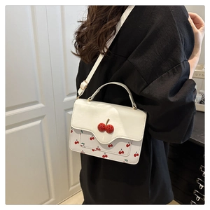 Detailed view of white crossbody bag with cherry prints and red 3D cherry buckle