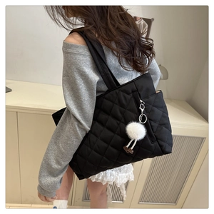 Close-up of black quilted tote bag with wide shoulder straps and plush charm