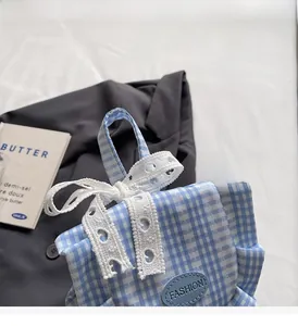 Detail of blue plaid fabric bag with white lace bow and fashion leather patch
