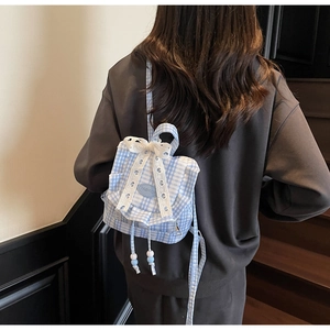 Dettaglio dello zaino a quadretti blu con pizzo bianco e un grande fiocco decorativo