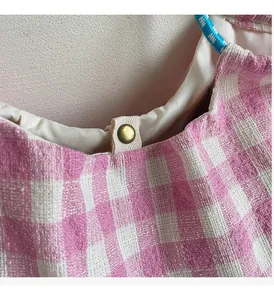 Detail of pink plaid tote bag featuring a vintage bronze snap button and woven texture