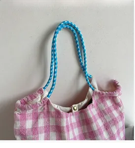 Detail of pink plaid tote bag with sturdy blue-white rope handles and gold snap button