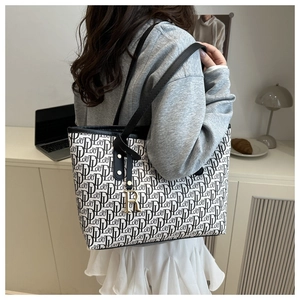 Detail view of large monogram tote bag with black straps and golden letter charm decoration
