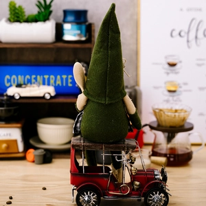 Gnom-Figur mit grünem Hut auf rotem Oldtimer vor gemütlicher Kaffee-Deko-Hintergrund