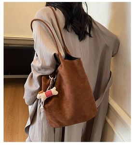 Close-up of brown suede tote bag featuring a cute cartoon dog plush charm and matte texture