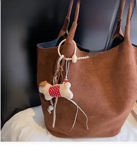 Close-up of brown suede tote bag with a cute puppy doll charm on a minimalist handle