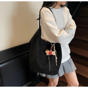 Detail of black suede tote bag with slim shoulder straps and a plush dog charm accessory