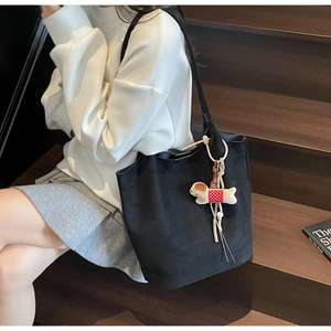 Detail of black suede tote bag with a cute plush puppy pendant on a vintage street background