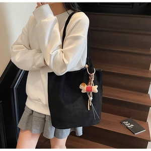 Detail of black suede tote bag with cute dog charm on female model with white hoodie
