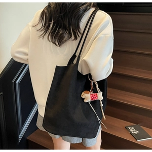 Detail of a large black suede tote bag with a cute white puppy plush charm on a shoulder strap