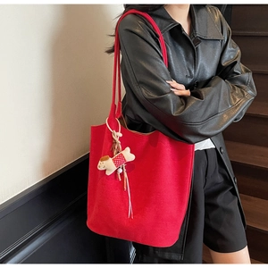 Close-up of red suede tote bag with a white dog charm on a model's shoulder