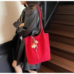 Detail of red suede tote bag with dog charm on long strap worn with black leather jacket