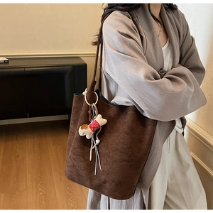 Detail of a large brown suede tote bag with a cute puppy plush charm on a side strap