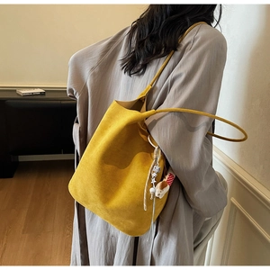 Detail of yellow faux suede bucket bag with long shoulder strap and cute puppy pendant