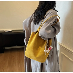 Detail of yellow suede tote bag with cute white dog charm on shoulder of a model