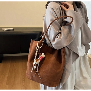 Close-up of brown suede tote bag featuring a cute plush dog pendant and long strap