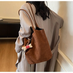 Side view of a brown suede tote bag worn by a model in a long coat with a cute charm