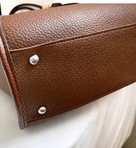 Detailed close-up of brown lychee leather tote bag bottom with protective metal studs