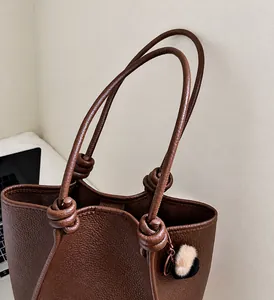 Detail of dark brown leather tote bag with decorative knot and textured lychee pattern